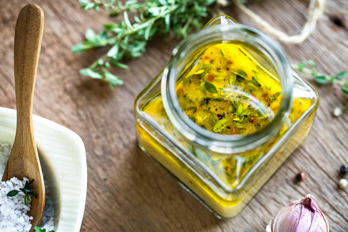 Herb-infused oil in glass jar with thyme, garlic, and sea salt on rustic wood—perfect for cooking or drinks.