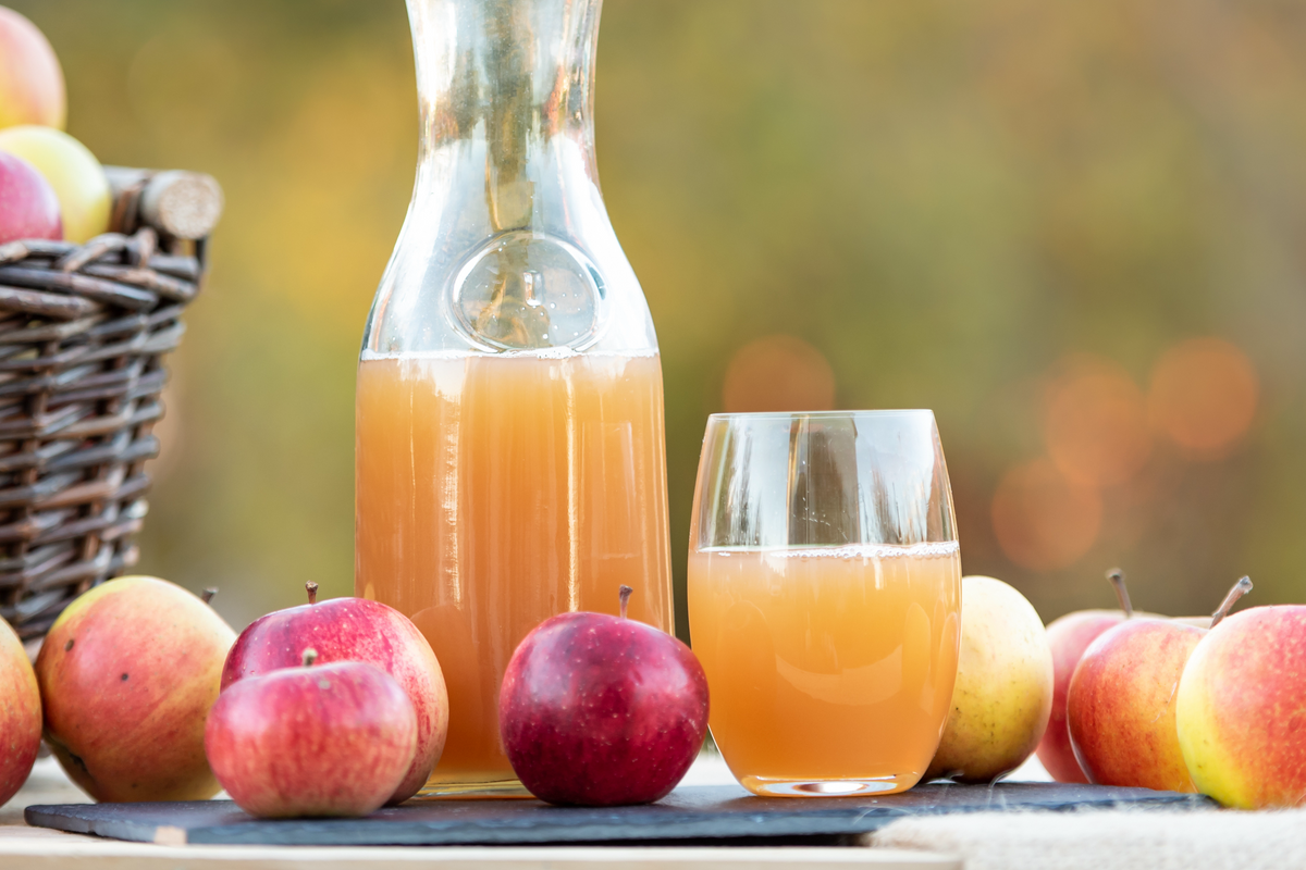 Apple Ginger Shrub in a glass carafe with fresh apples and a finished drink.
