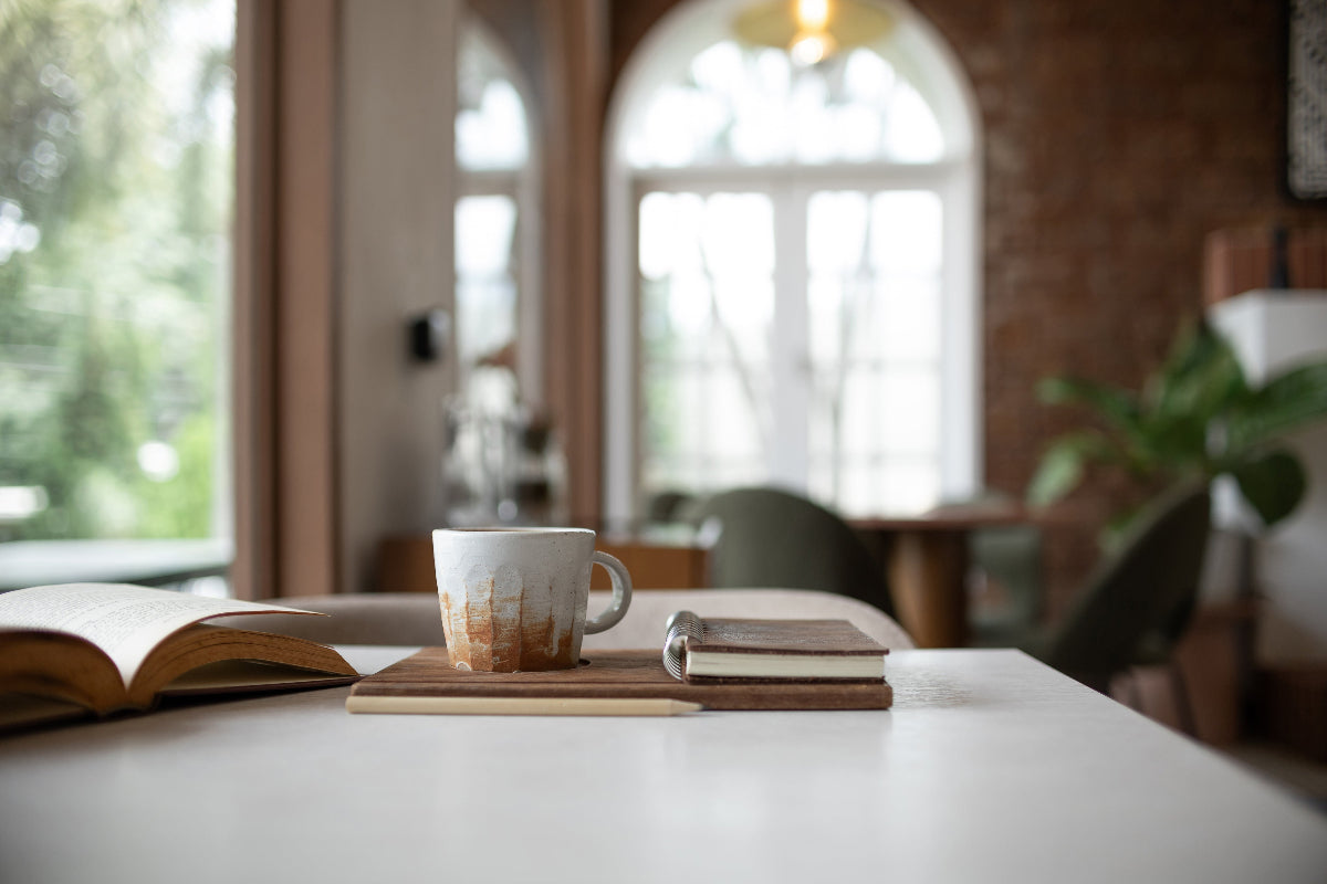 Cozy cafe table with ceramic mug, open book, and notebook near arched window