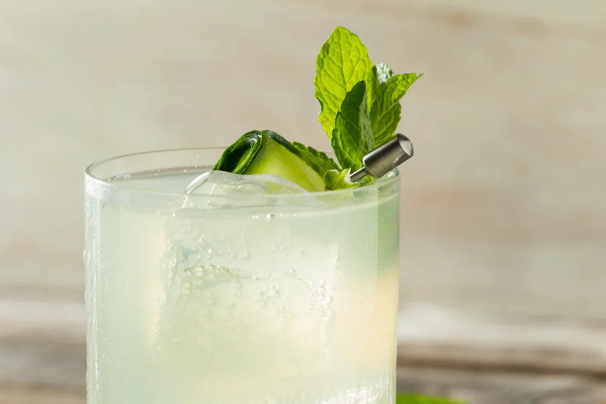 Cucumber lime cooler with mint garnish in a glass over ice on a rustic wooden surface