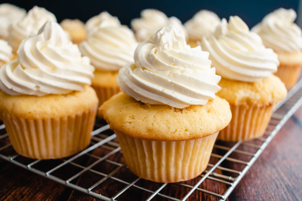 Frosted vanilla cupcakes cooling on a wire rack before adding cannabis drops to the frosting
