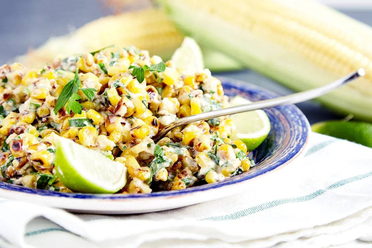 Grilled corn salad with lime wedges, fresh herbs, and charred sweet corn in a serving bowl