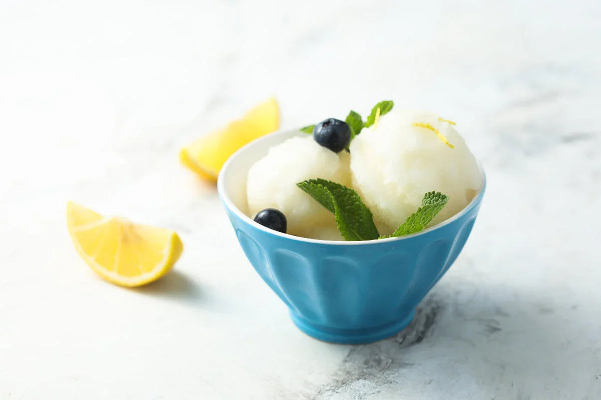 Homemade lemon sorbet with fresh blueberries, mint, and lemon zest served in a blue bowl with fresh lemon wedges.