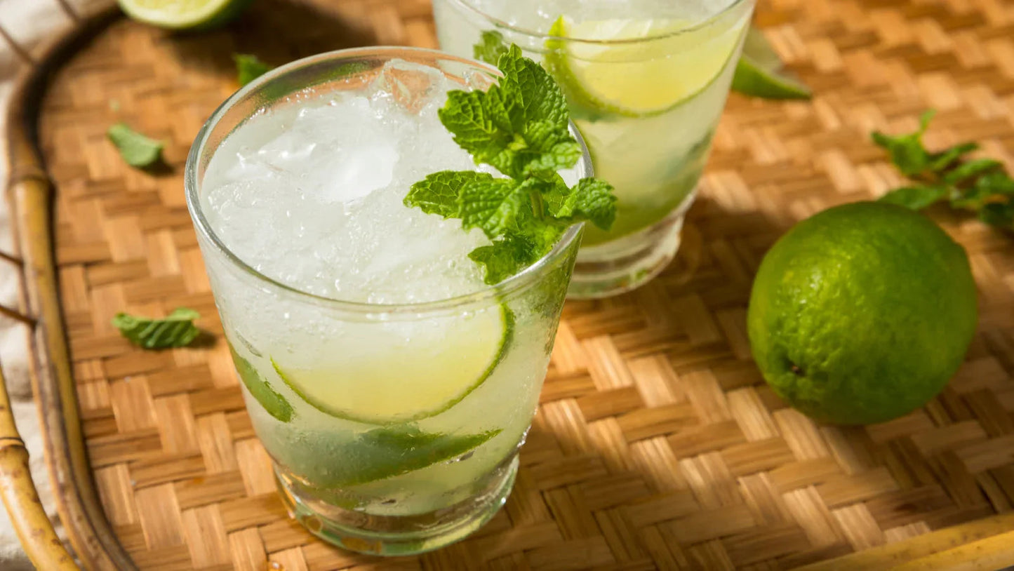 Refreshing mojito cocktail with lime slices and mint leaves on a woven tray, perfect for bar or kitchen use.