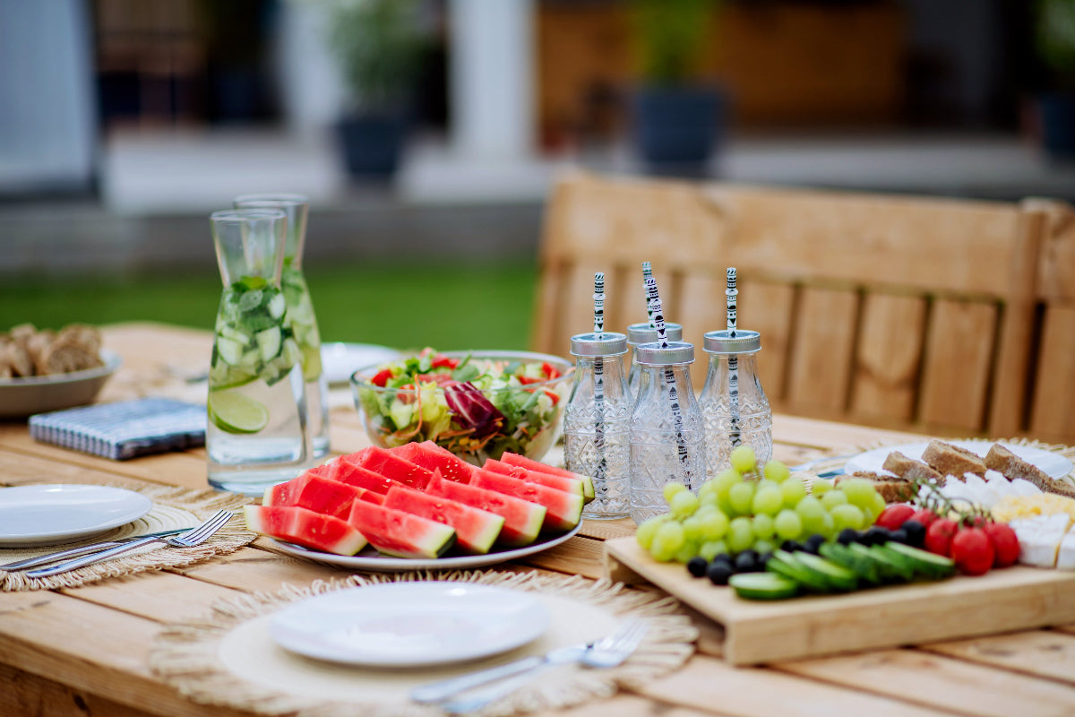 Outdoor table set for home entertaining with a charcuterie board, fresh fruit, salad, and sparkling drinks.