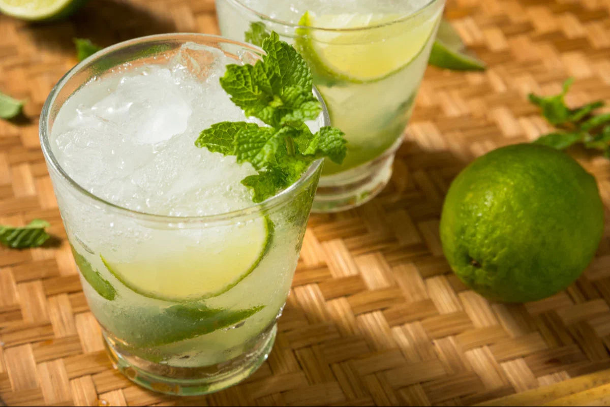 Refreshing mojito cocktail with lime slices and mint leaves on a woven tray, perfect for bar or kitchen use.