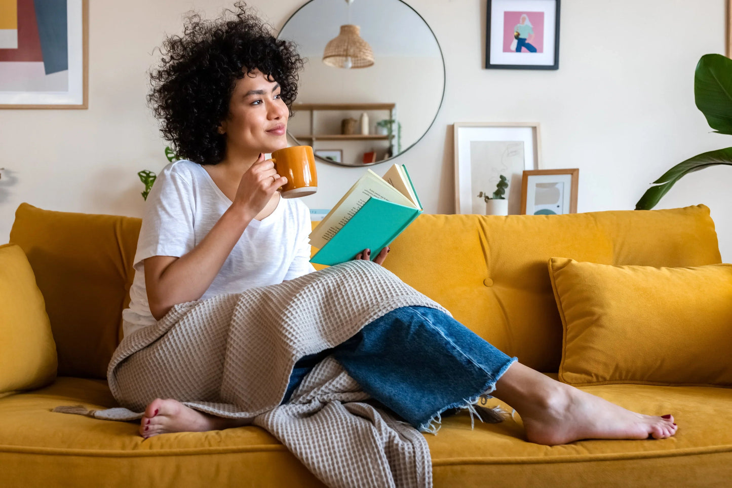 Woman relaxing on yellow couch with book and mug, enjoying calm moment at home