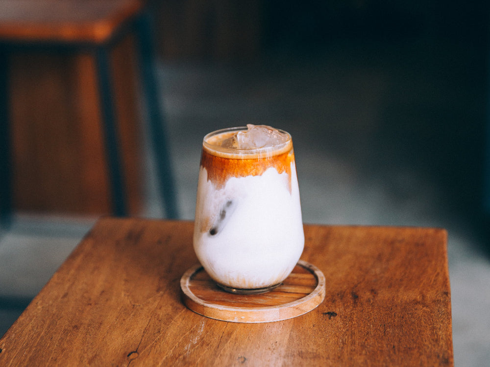 Two-layered coffee cream infused drink in a glass on a wooden table with a blurred background