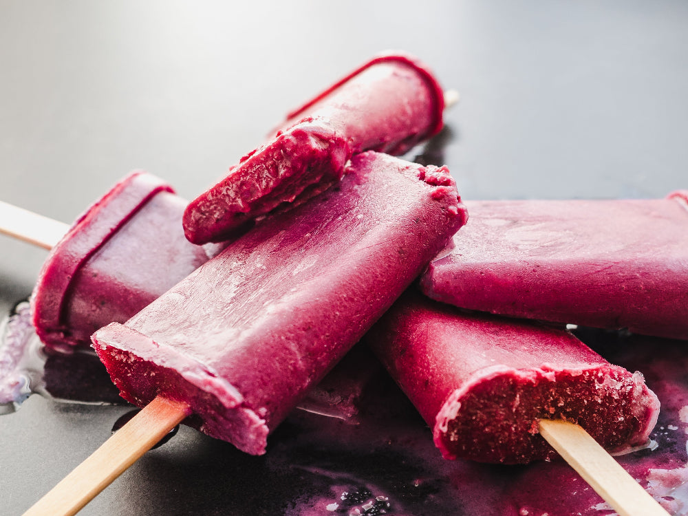 infused berry popsicles on a gray surface with a blurred background