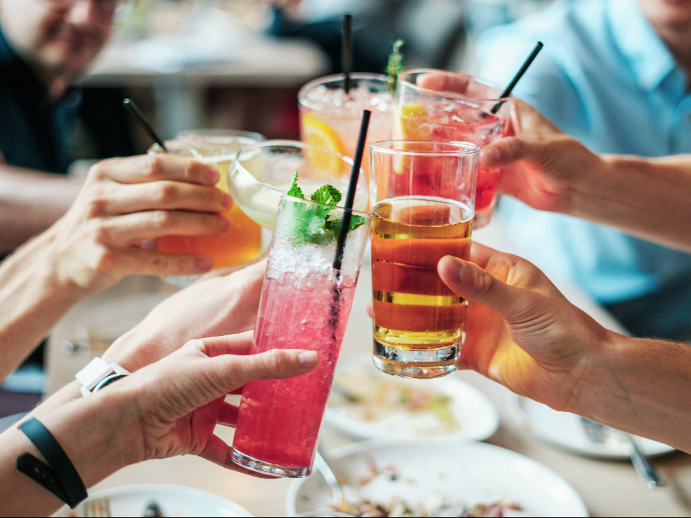 People toasting with colorful drinks at a restaurant.