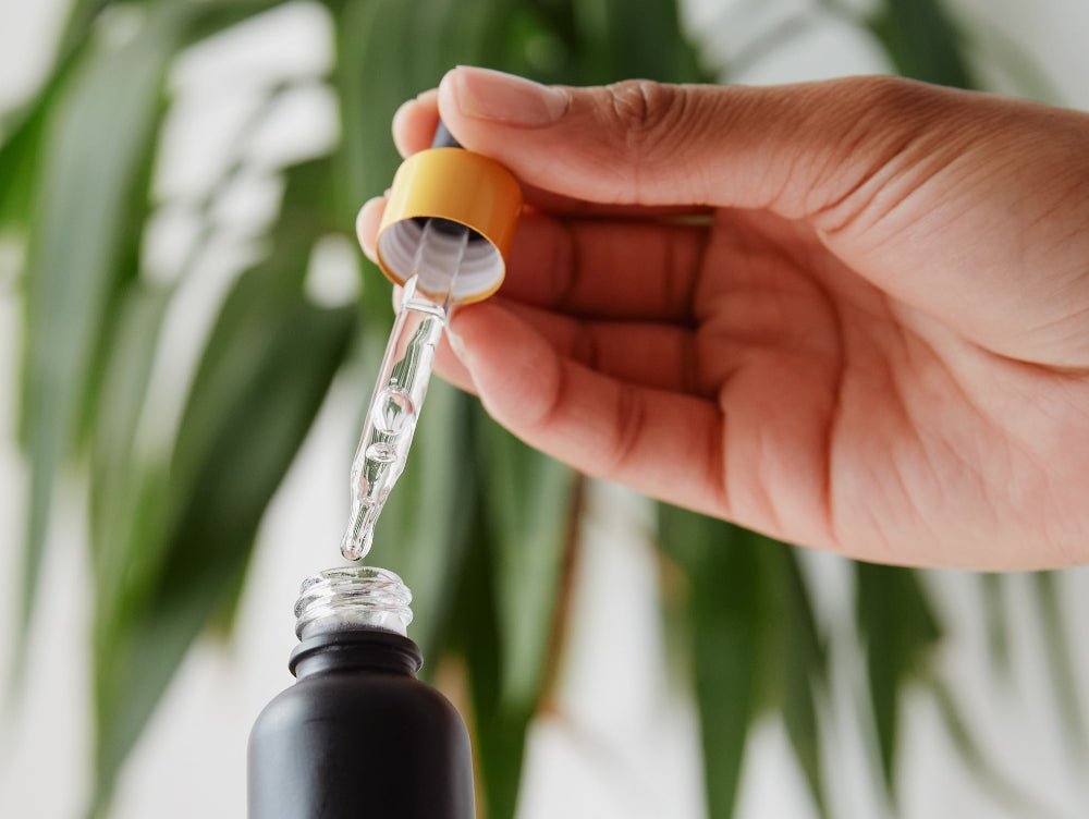 Hand holding a dropper with a blurred green plant background