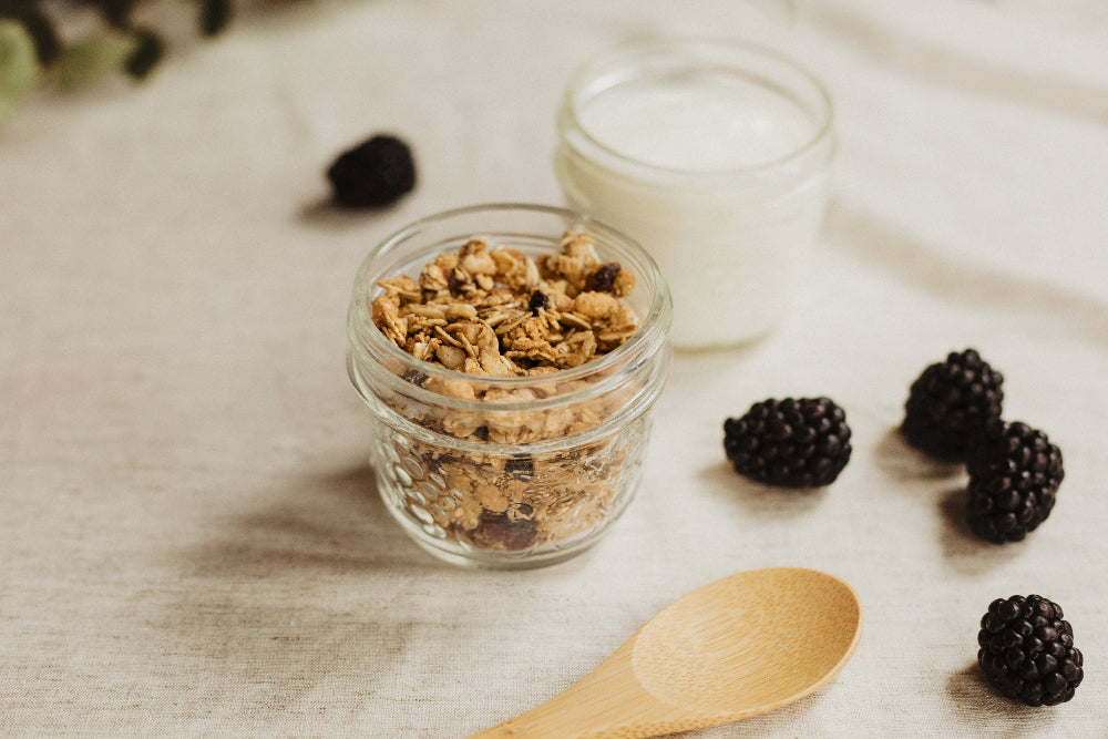 Jar of granola with blackberries and a wooden spoon on a light surface