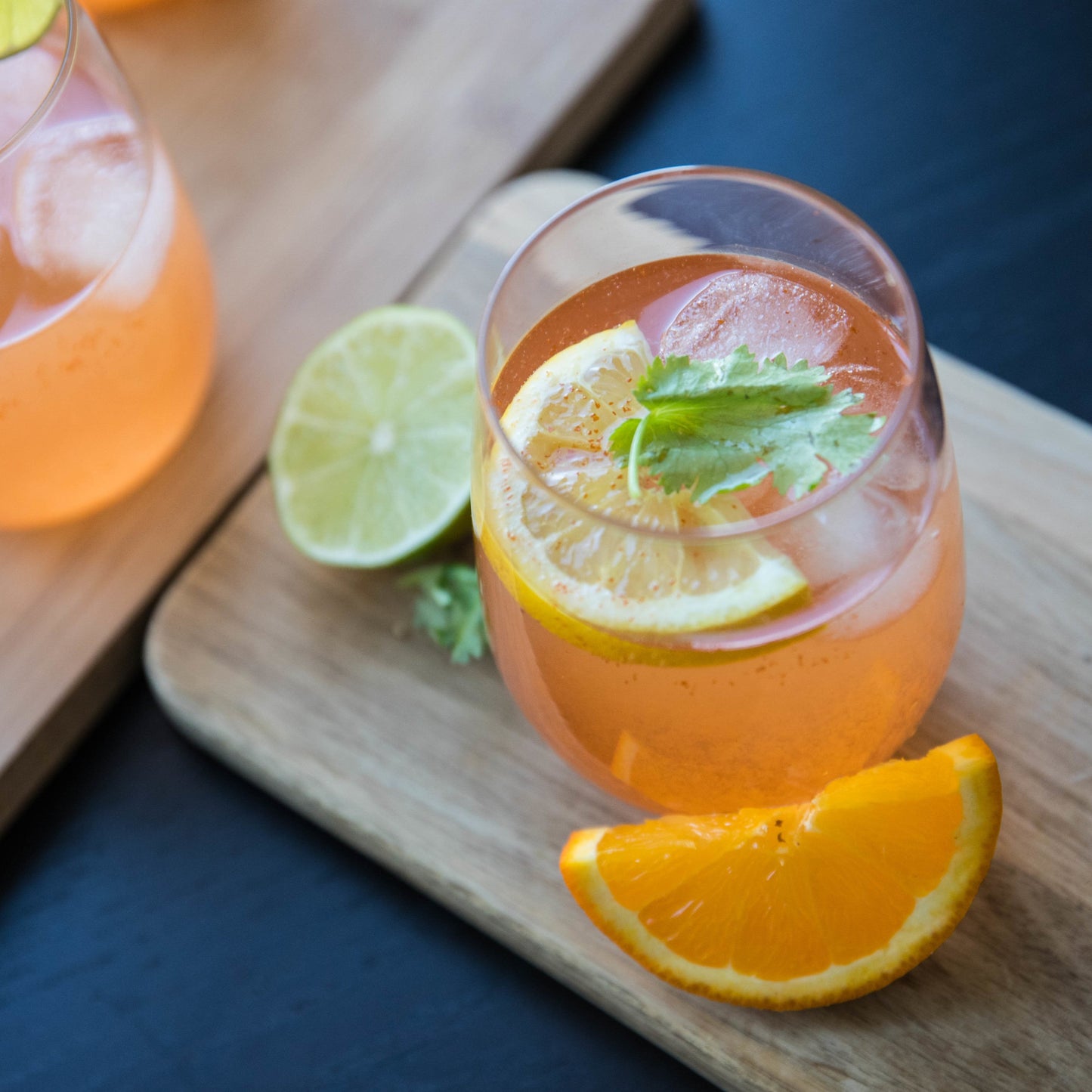 Two glasses of orange mocktail with lemon slices and ice on a wooden board.