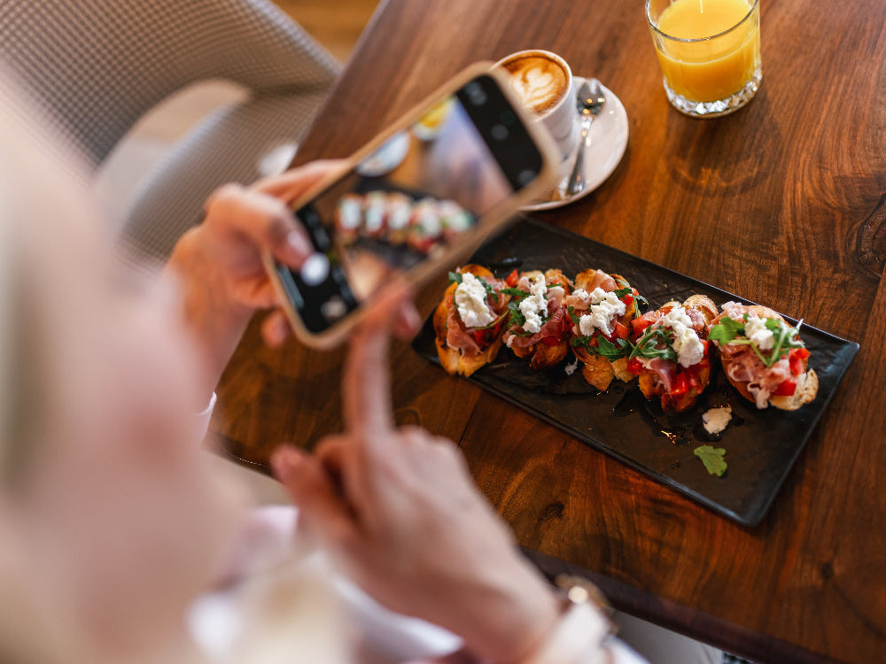Person taking a photo of a plate of food with a smartphone on a wooden table.