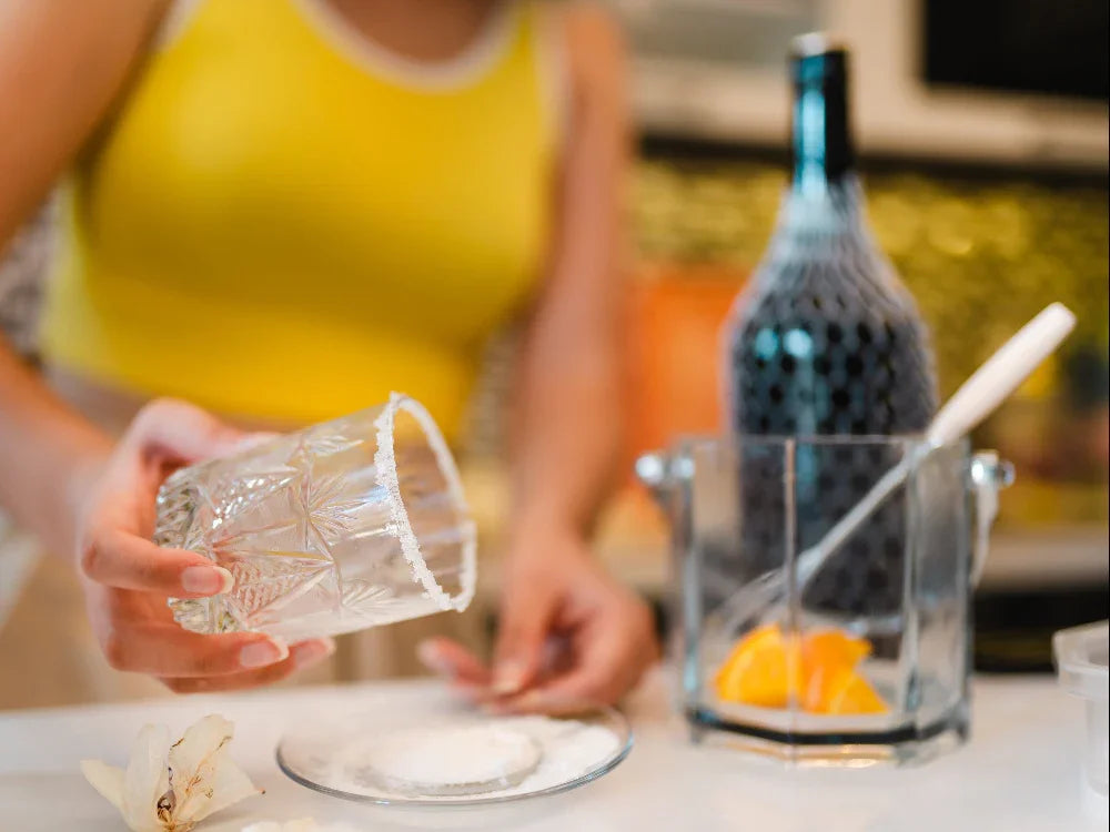 Preparing a salt-rimmed citrus mocktail with fresh orange and bar tools.