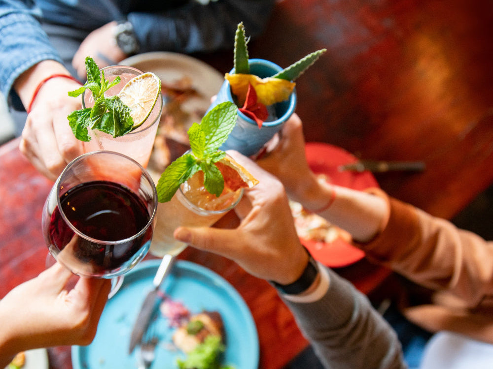 Friends toasting with colorful cocktails and wine at a lively table gathering